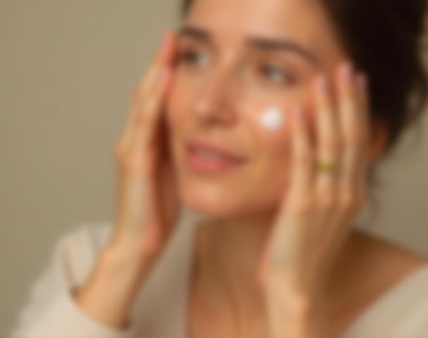 Hands applying skincare product to a face.